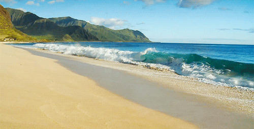 A tropical beach with waves rolling onto the sand below green mountains
