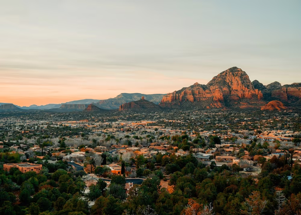 Sunset view of a town with red rock mountains in the background under a pastel sky.