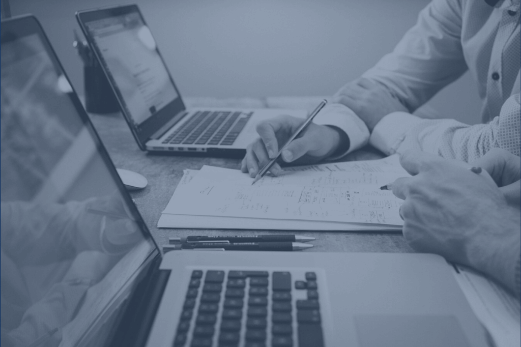 Two people reviewing printed financial documents at a desk with a laptop